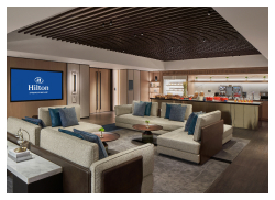 A sophisticated lounge area with plush seating, a large screen displaying the Hilton logo, and a buffet counter in the background.