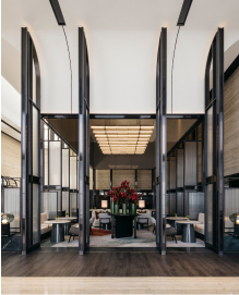 Elegant interior with a series of dark door frames leading to a seating area adorned with a red floral centerpiece; modern lighting hanging above.